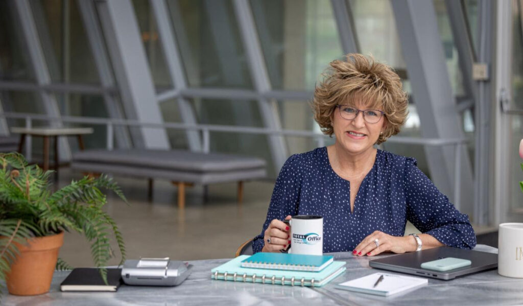 Shelley Carnahan sat at desk holding a mug of coffee